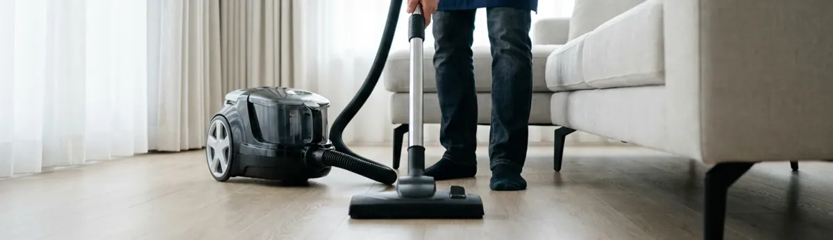 Professional house cleaner vacuuming a living room floor with a canister vacuum cleaner, Arvada, CO.