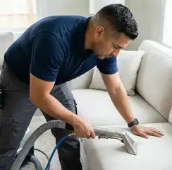 Professional upholstery cleaning technician using an extraction wand to deep-clean a fabric sofa, Arvada, CO.